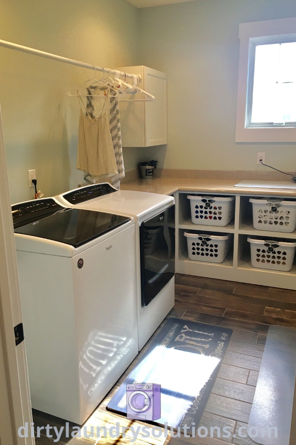 A small laundry room showing a washer and dryer, a folding counter, and storage solutions, designed for efficiency and coziness, featuring wood-looking tile and painted in Sherwin Williams Sea Salt. Discover inspiring ideas for your home at dirtylaundrysolutions.com.