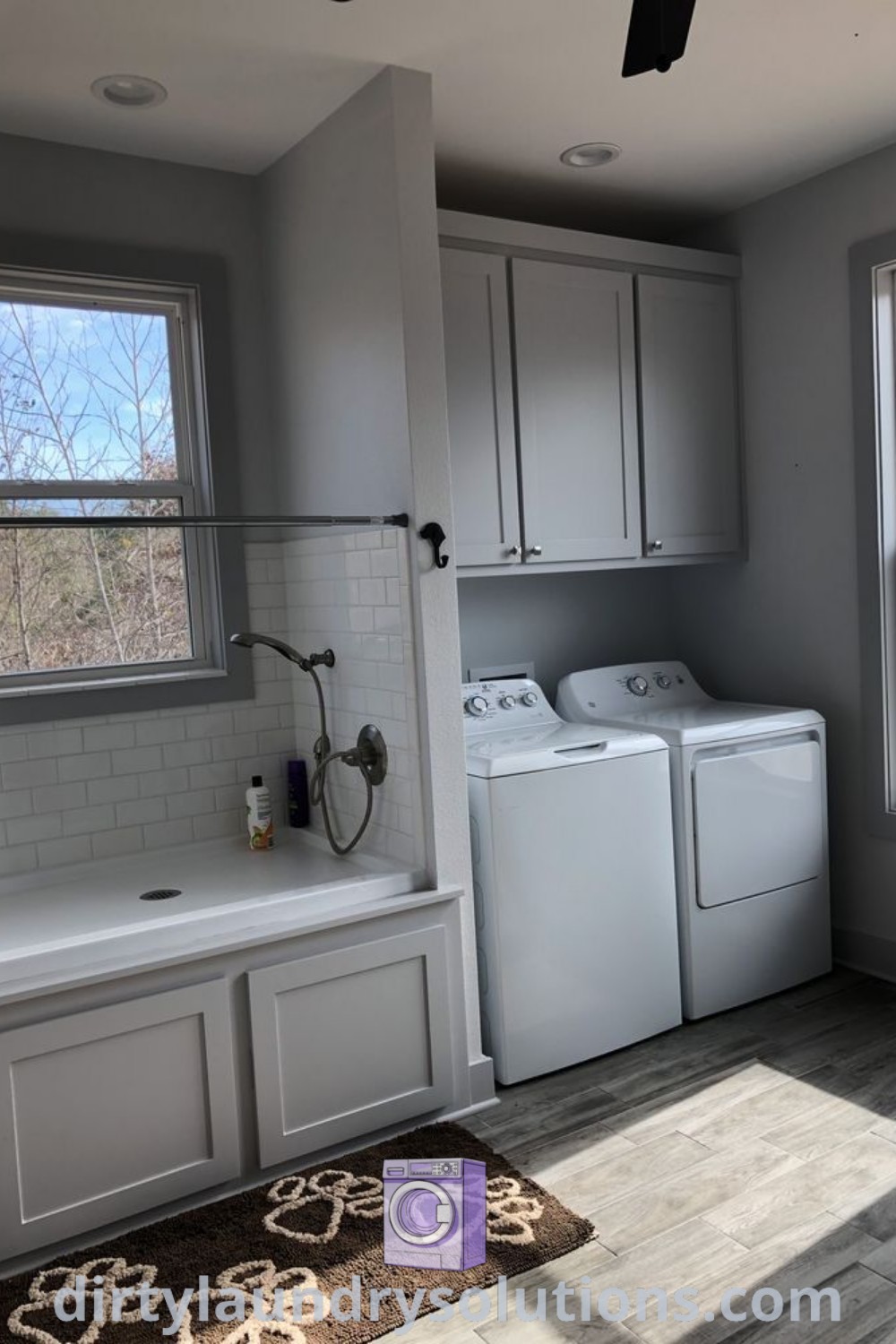 A washer and dryer placed next to a window in a cozy laundry room with a rug, featuring cabinets and stylish decorations for effective organization. Discover laundry renovation ideas and solutions at dirtylaundrysolutions.com.