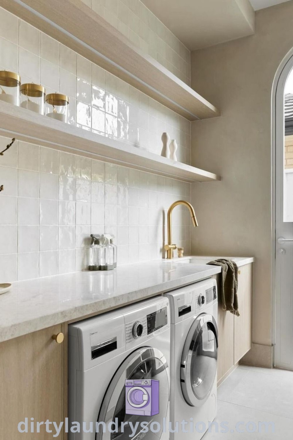 A stylish laundry room with a washer and dryer on white tile walls and open shelving, blending scandi utility room aesthetics and Mediterranean laundry room inspirations. Discover more organizational ideas at dirtylaundrysolutions.com.