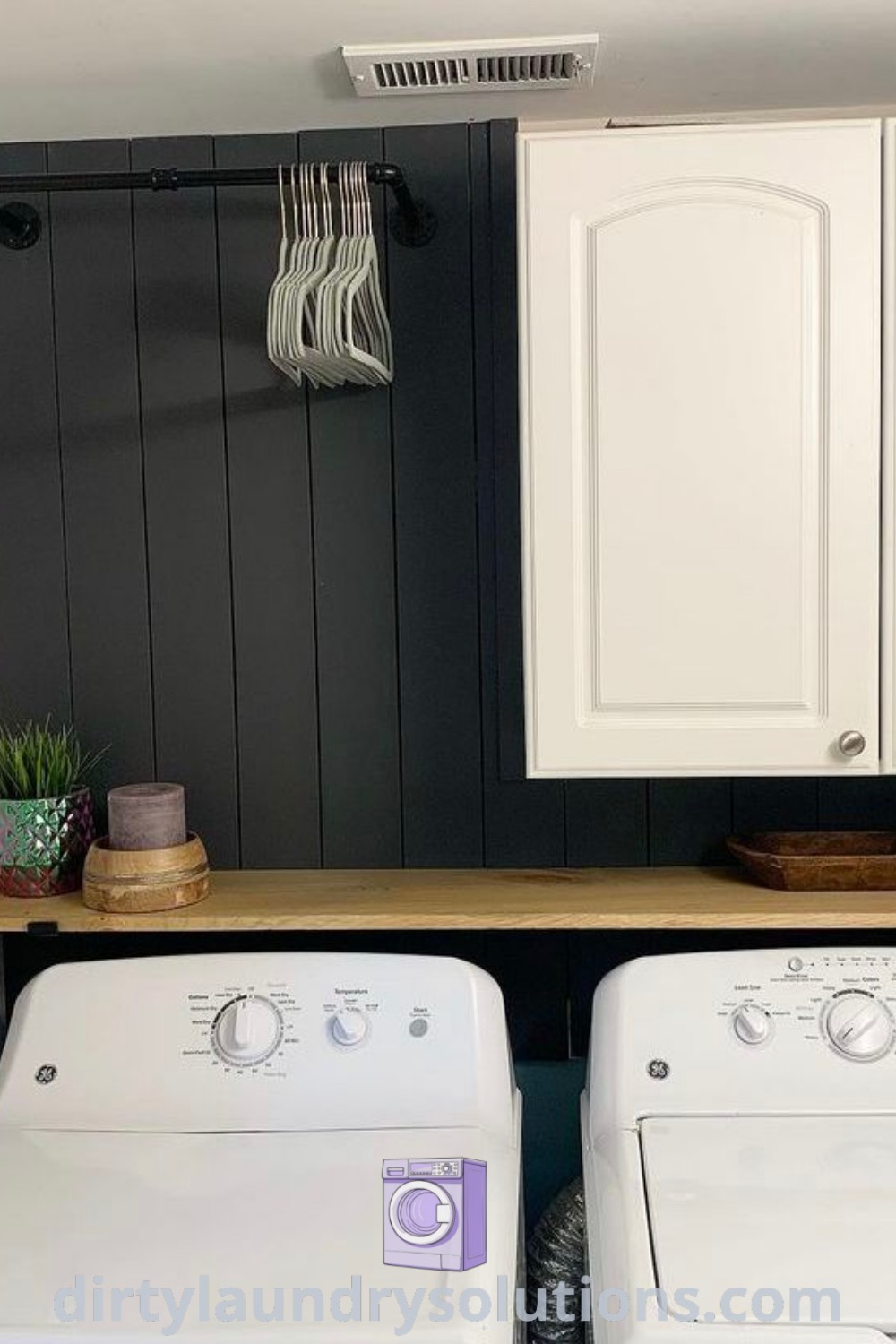 Two white washers in a laundry room with black walls, showcasing a cozy aesthetic with a black accent wall. Discover unique ideas for black laundry rooms and small space solutions at dirtylaundrysolutions.com.