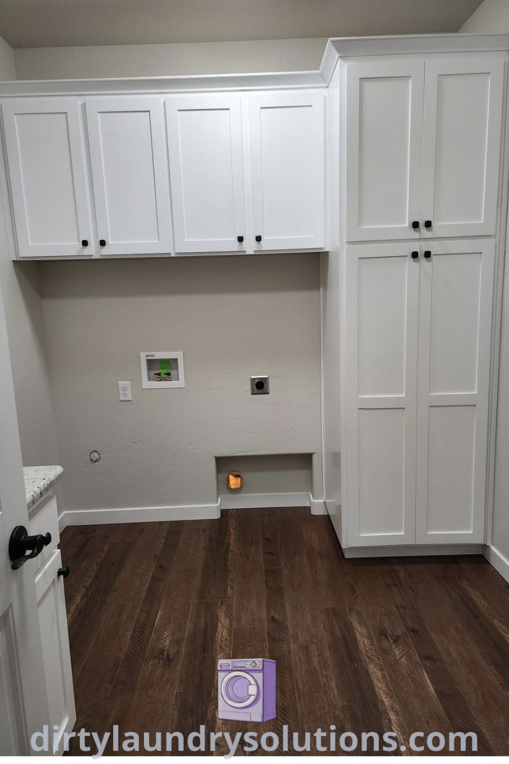 An empty laundry room with white cabinets, wood floors, and organized storage spaces including cupboards for cleaning supplies and a broom closet. Discover more inspiring laundry room ideas and solutions at dirtylaundrysolutions.com.