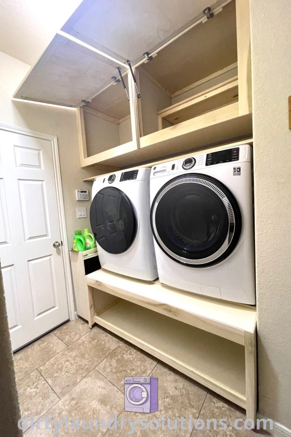A cozy laundry room featuring a raised washer and dryer, stylish upper cabinets, and tile flooring, showcasing effective organization and aesthetic appeal. Discover innovative laundry room cabinet ideas, solutions for small spaces, and more at dirtylaundrysolutions.com.