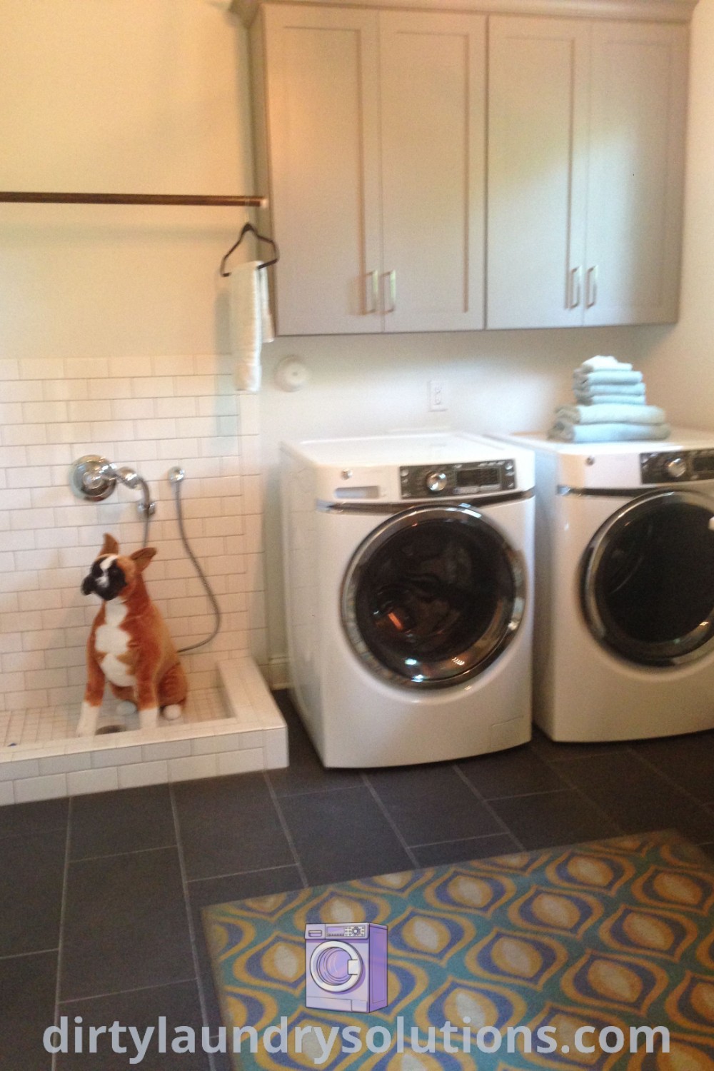A bathroom with a washer and dryer and a cozy dog washing station, featuring a dog sitting on the floor, showcasing functional design ideas for dog homes. Discover unique solutions for laundry room inspiration and pet care at dirtylaundrysolutions.com.