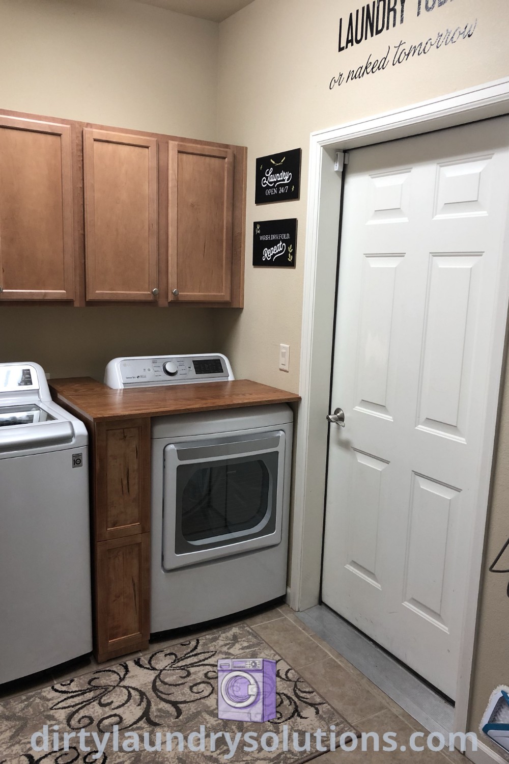 A washer and dryer positioned in a cozy laundry room next to a white door, featuring a folding table, ironing board, and stand-up freezer, showcasing efficient design ideas for small spaces. Discover more unique ideas and solutions at dirtylaundrysolutions.com.