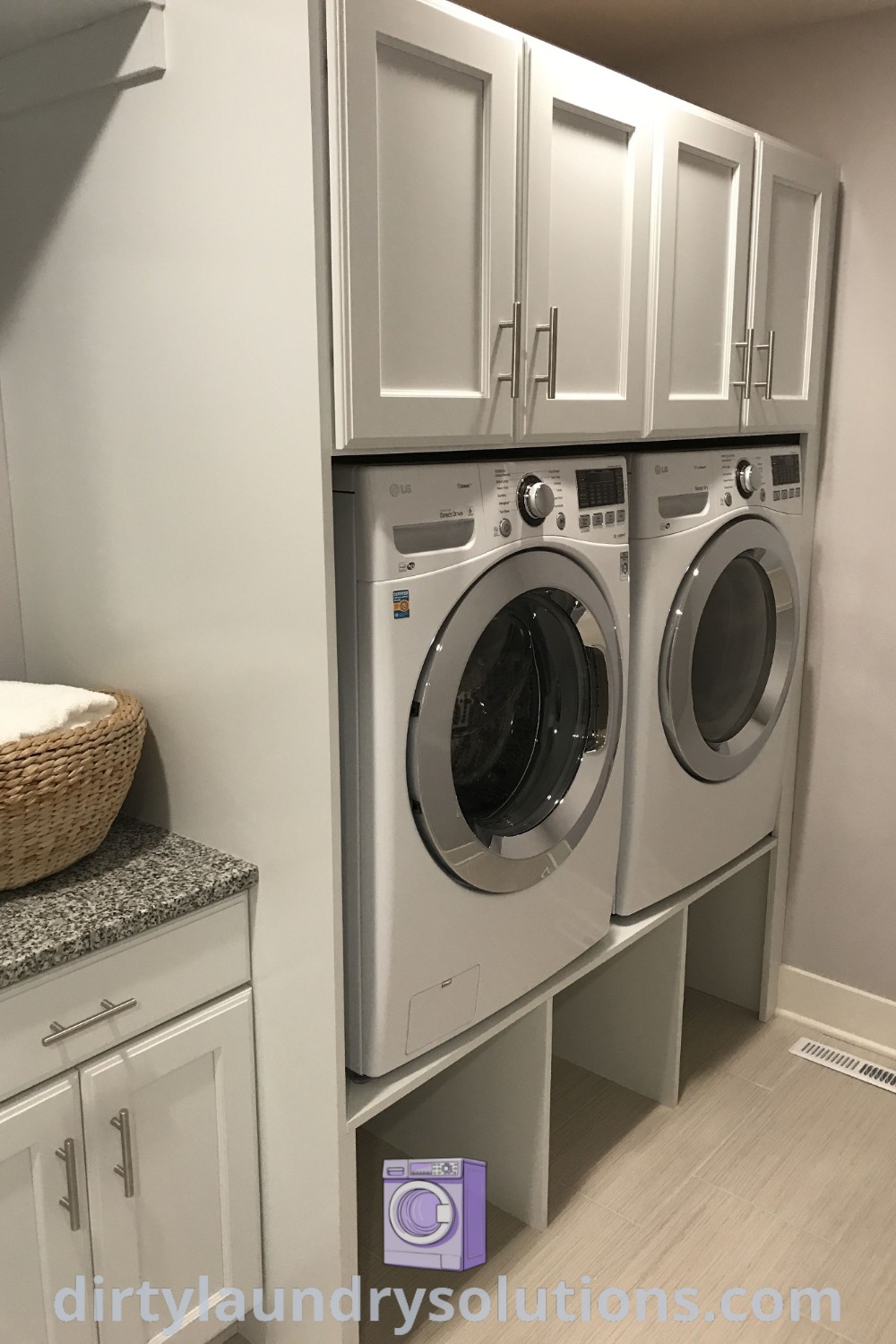 A washer and dryer in a white laundry room featuring built-in cabinets, showcasing under laundry machine storage and laundry baskets under the washer. Discover practical solutions for organizing your laundry space at dirtylaundrysolutions.com.
