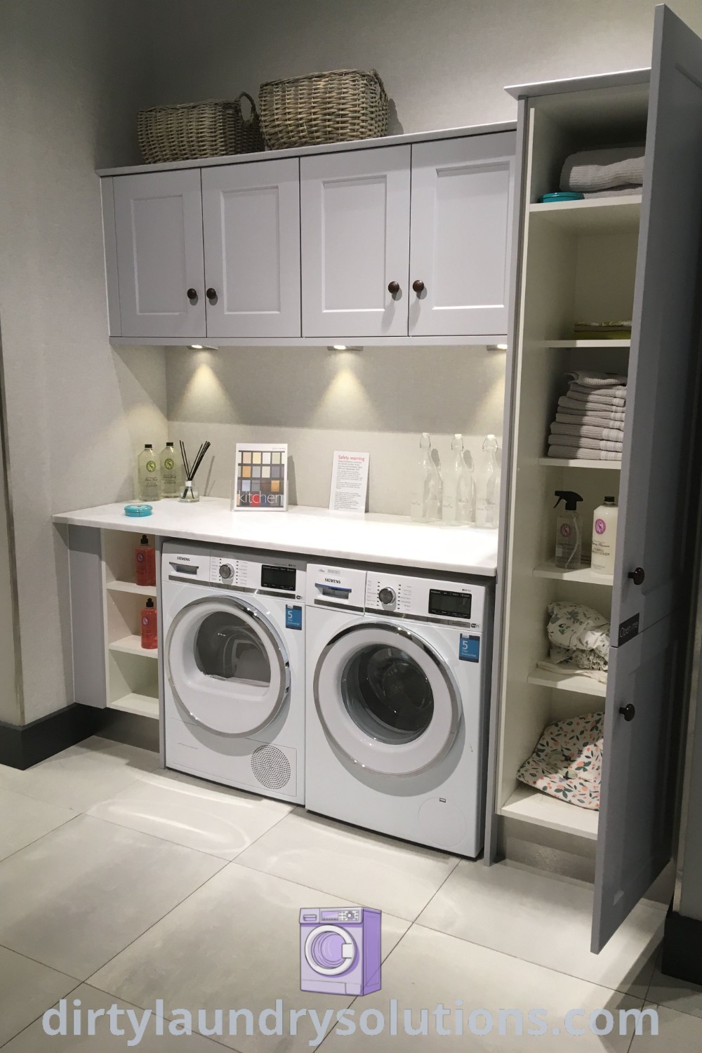 A utility room featuring a washer and dryer with built-in shelving on white tile flooring, showcasing stylish laundry room ideas and organization solutions. Discover more inspiring concepts for your cozy home at dirtylaundrysolutions.com.