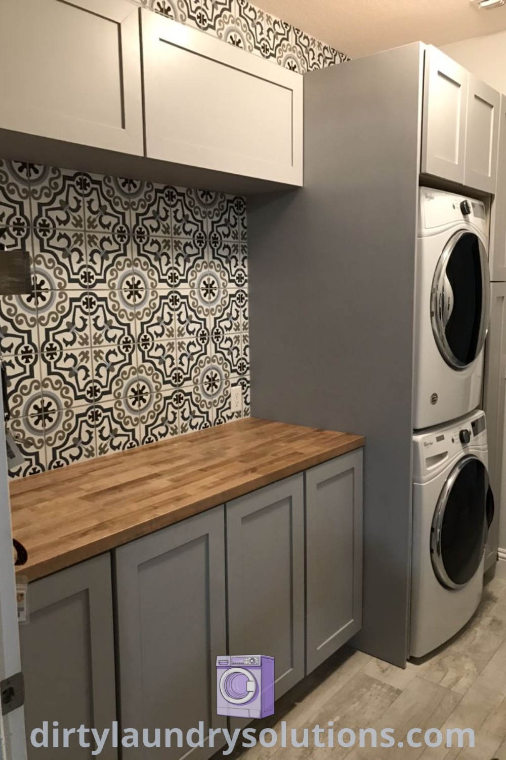 A stacked front loader washer and dryer in a kitchen arranged on top of cabinets, complemented by organized storage options and basket solutions. Discover cozy and functional laundry room ideas at dirtylaundrysolutions.com.