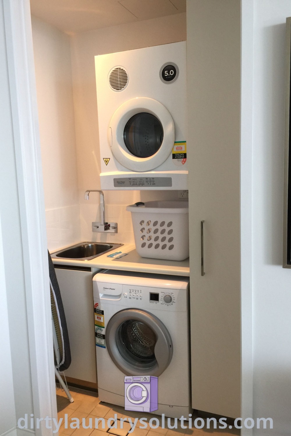 A cozy laundry room with a washer and dryer next to a wall-mounted painting, showcasing small apartment laundry solutions and contemporary design ideas. Explore creative laundry addition inspiration and organization tips at dirtylaundrysolutions.com.