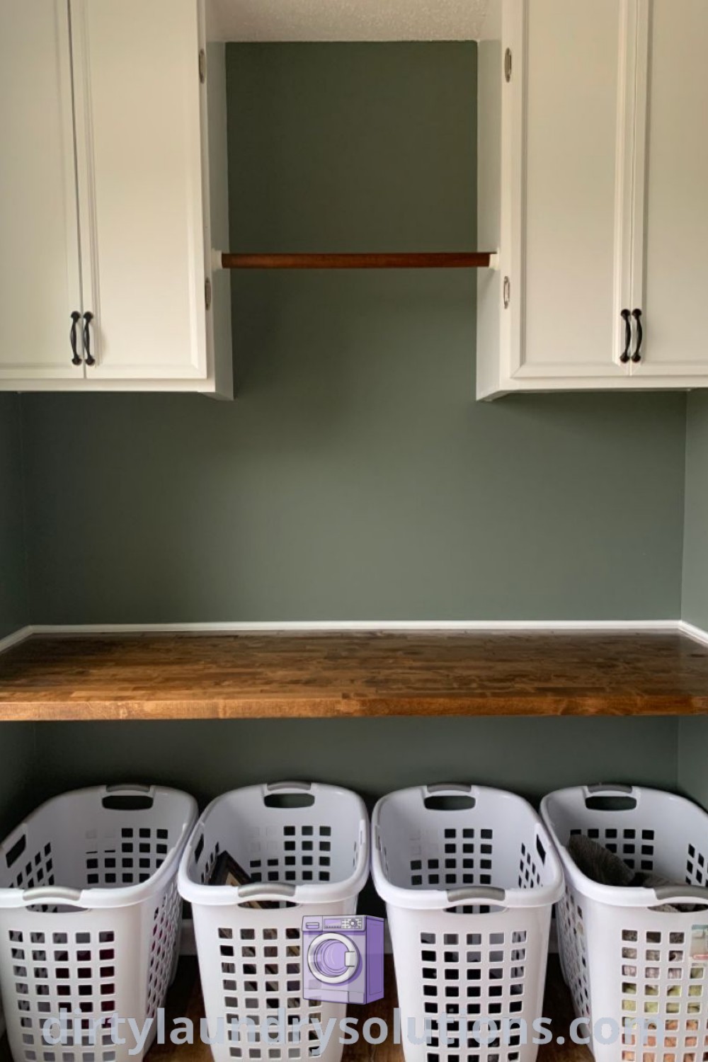 A cozy and well-organized laundry room under the stairs in olive green, featuring stackable machines and clever storage ideas. Explore unique solutions for busy homes and small spaces at dirtylaundrysolutions.com.