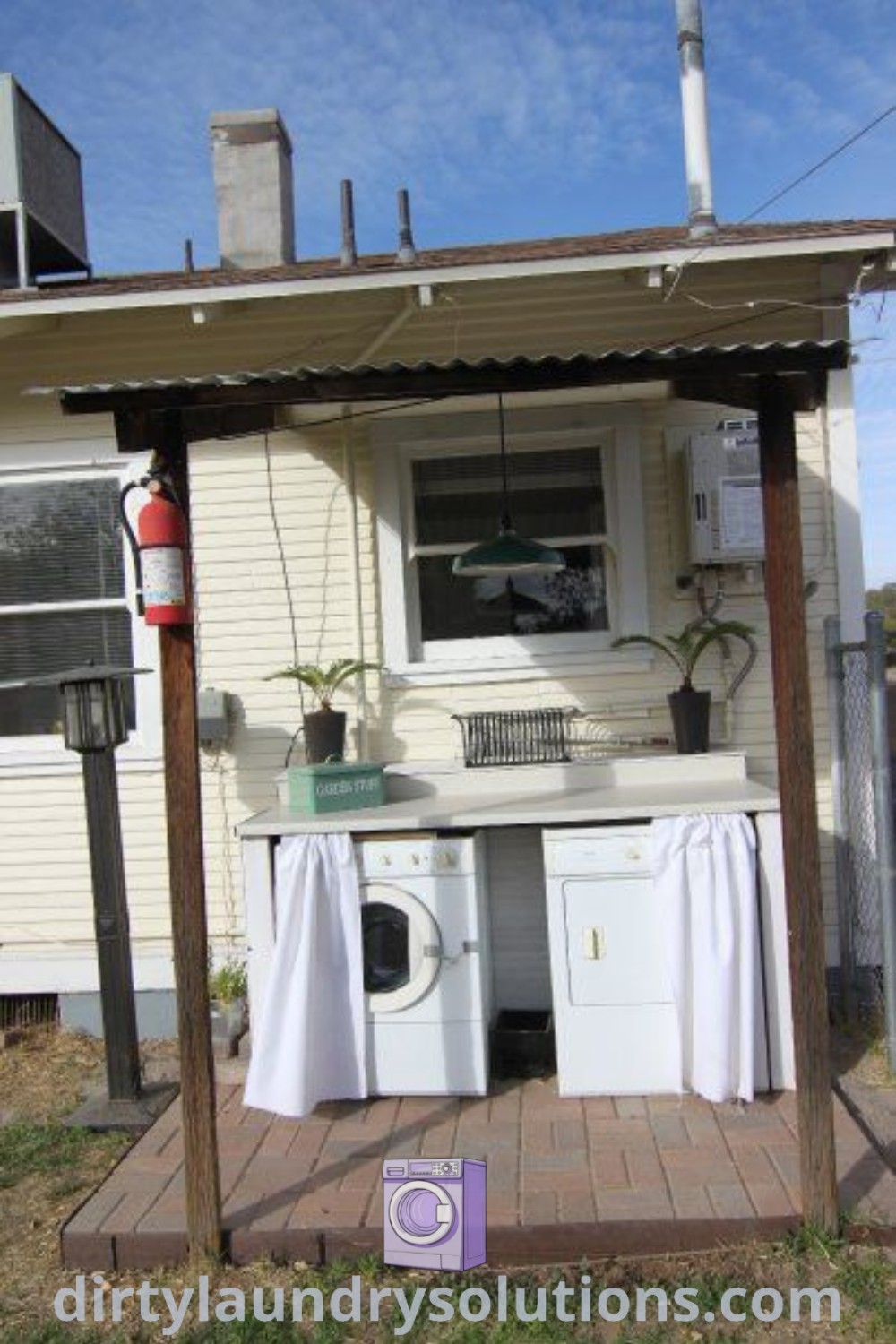 A small house with a washing machine in the front yard and an outside kitchen area, highlighting an outdoor laundry setup. Explore cozy ideas and organization solutions for laundry at dirtylaundrysolutions.com.