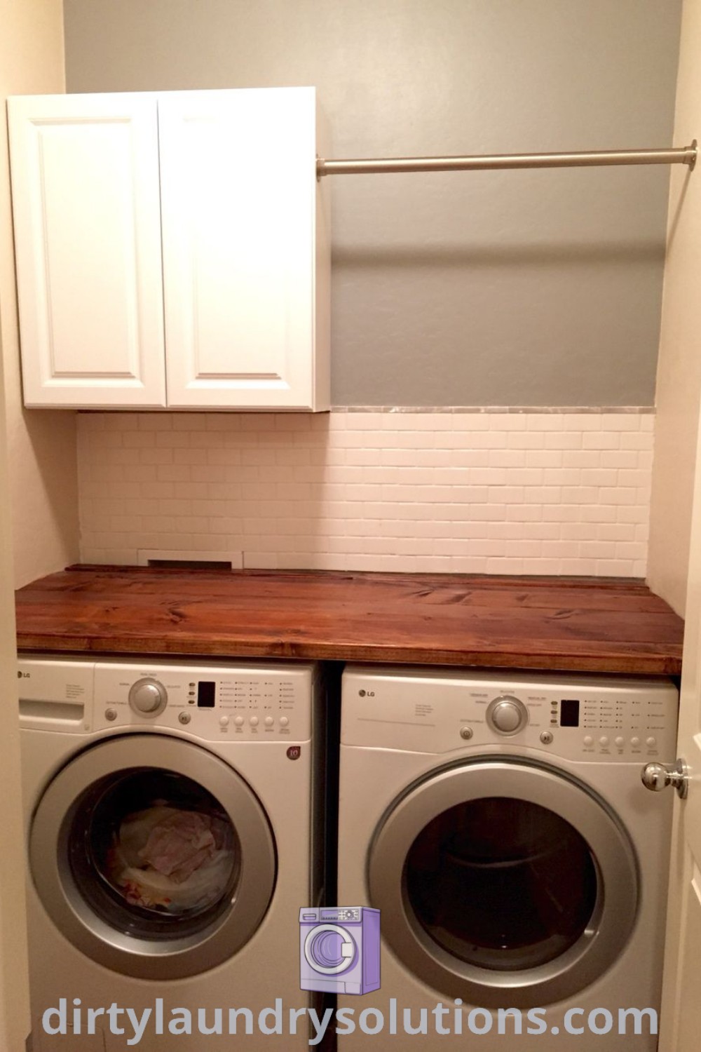 A small corner laundry room featuring a washer and dryer, white cabinets on the wall, and stylish decor, showcasing inspiring ideas for small spaces. Discover more unique organization ideas and cozy aesthetics at dirtylaundrysolutions.com.