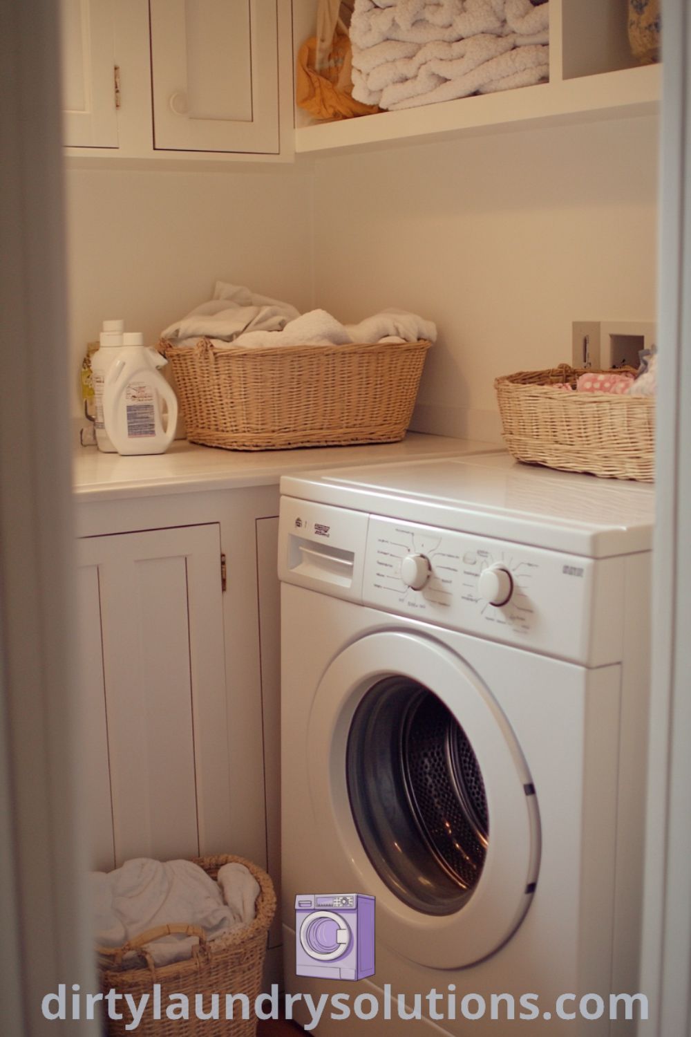 Cozy laundry room nook featuring a washer and dryer between white cabinets, organized baskets on shelves, and soft lighting illuminating textured surfaces and worn tiles. Explore unique ideas for your home at dirtylaundrysolutions.com.