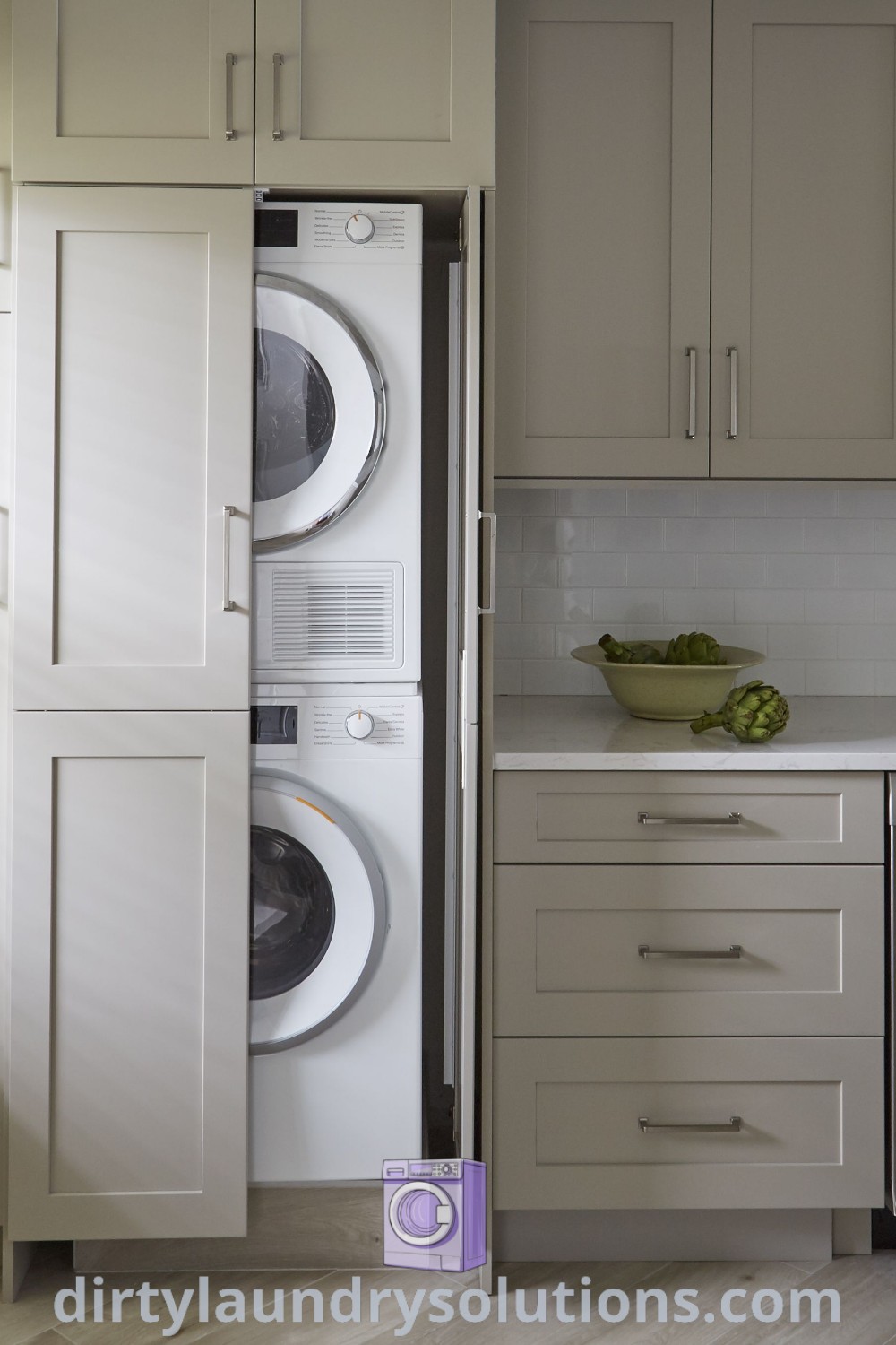A modern kitchen showcasing a washer and dryer on top of built-in cabinets, demonstrating stylish laundry appliance solutions. This layout emphasizes organization ideas and cozy aesthetics, featuring designs from dirtylaundrysolutions.com.
