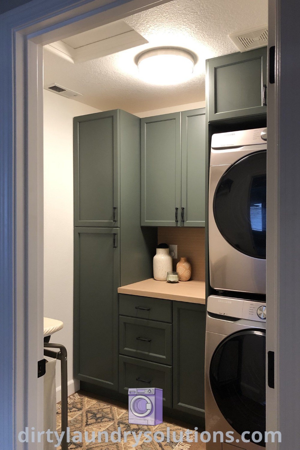 A cozy kitchen with green cabinets featuring a corner oven, stacked washer and dryer, and organization ideas for a functional pantry and laundry room design. Discover unique solutions and inspirations for small spaces at dirtylaundrysolutions.com.