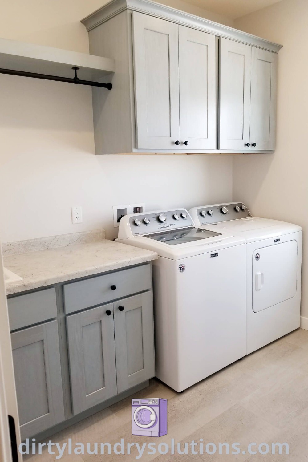 A cozy small laundry room featuring a white washer and dryer, overhead cabinets, and a hanging rack, showcasing effective organization ideas for small spaces. Discover more laundry room inspirations and solutions at dirtylaundrysolutions.com.