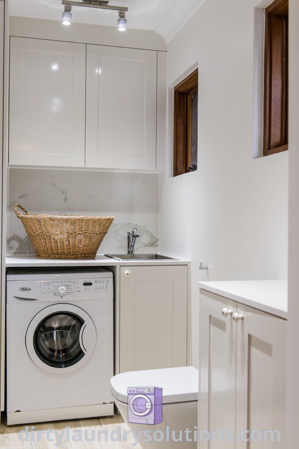 A cozy laundry room with a washer and dryer, white cupboards, and a toilet, offering solutions for small utility and toilet combos. Discover inspiring ideas for efficient small spaces at dirtylaundrysolutions.com.