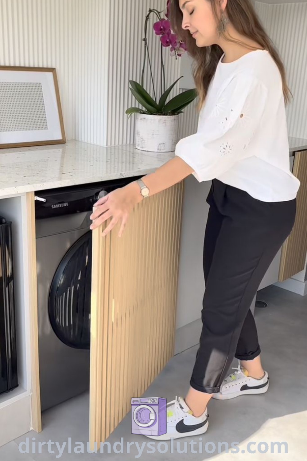 A woman stands in front of a hidden washing machine in a kitchen, showcasing stylish solutions for hiding washing machines. Explore washing machine cover ideas and laundry room designs at dirtylaundrysolutions.com.