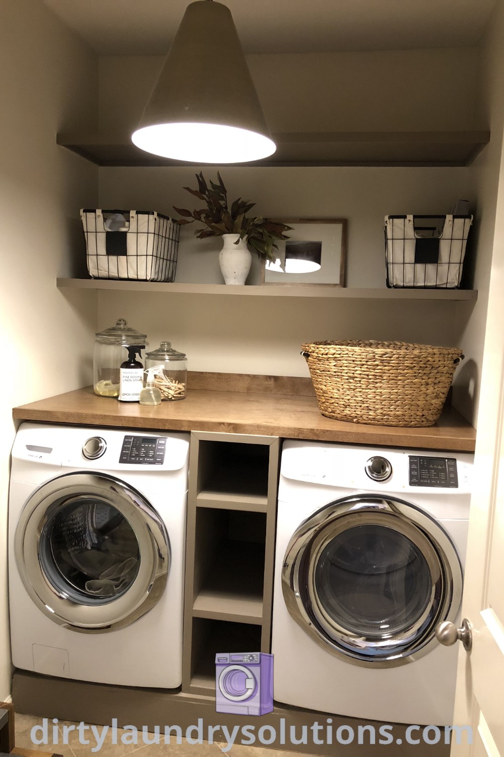A small laundry room featuring a washer and dryer with storage baskets on an overhead shelf, demonstrating efficient design ideas for cozy homes. Discover more inspiring organization ideas for small spaces at dirtylaundrysolutions.com.