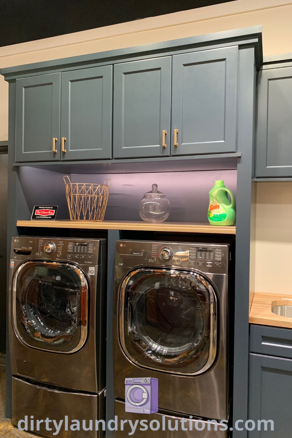 A navy blue laundry room with a washer and dryer, blue cabinetry, and a cozy aesthetic, featuring design ideas for efficient organization and a dog wash area. For more inspirations, visit dirtylaundrysolutions.com.