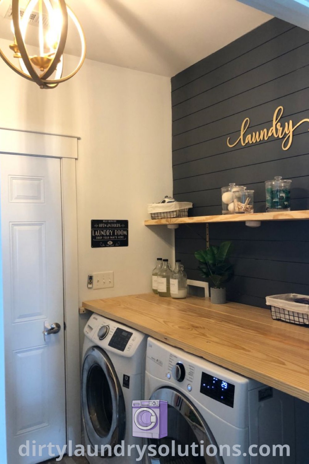A stylish small laundry room with a black wall and a washer and dryer next to a door labeled 