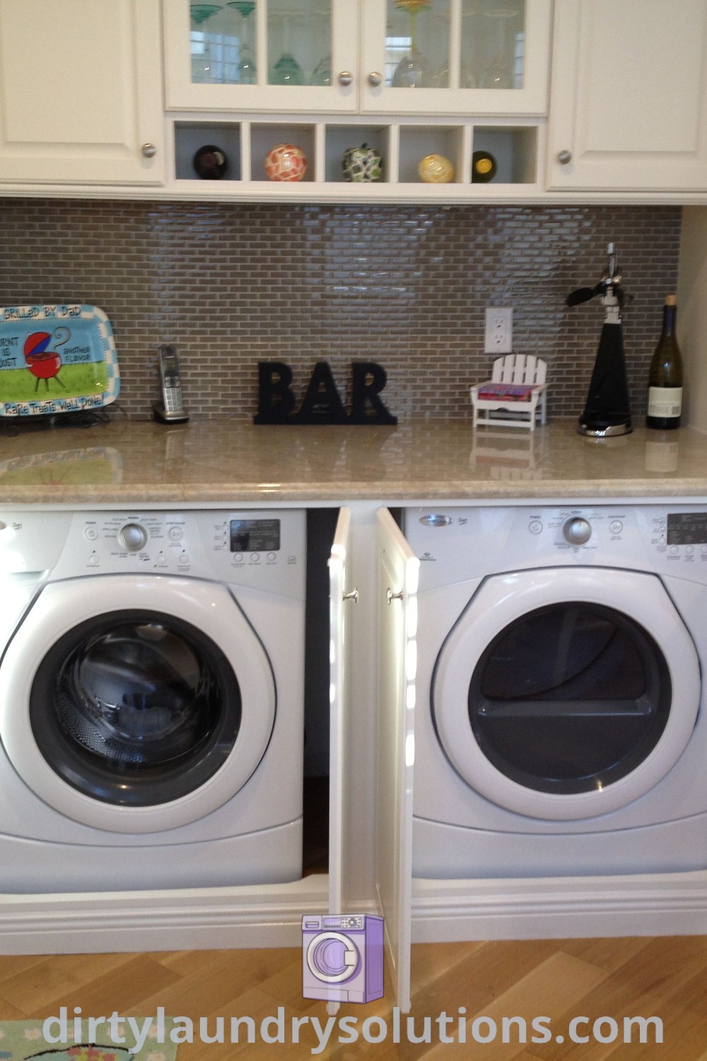 A cozy kitchen featuring an under counter washer and dryer in a tidy room with white cabinets and wood flooring, showcasing laundry area in kitchen ideas. Explore more inspiring solutions at dirtylaundrysolutions.com.