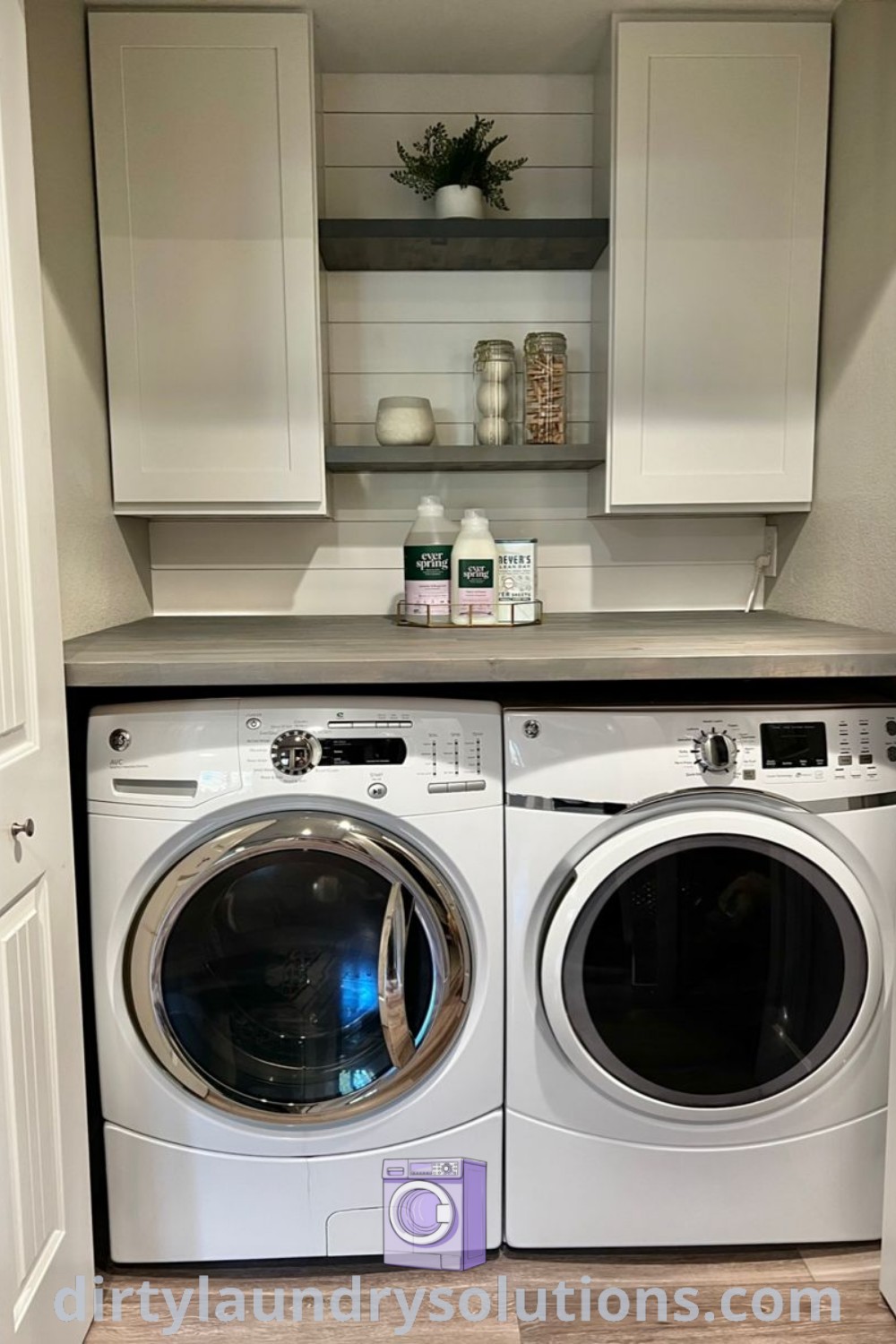 A small laundry room featuring a gray washer and dryer with white cupboards on the wall, highlighting cozy organization ideas and design inspirations for busy homes. Discover more laundry room solutions at dirtylaundrysolutions.com.