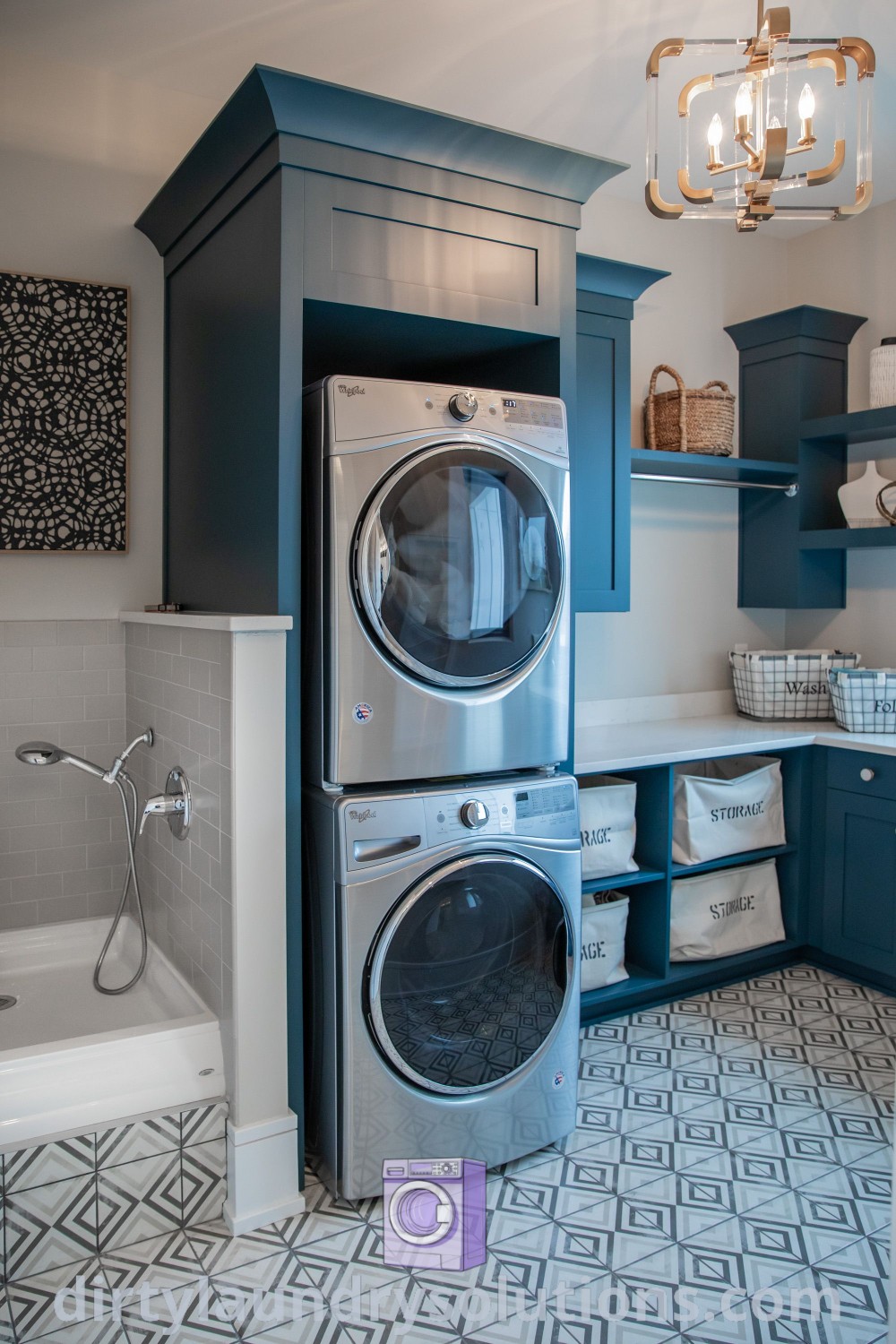 A stackable washer and dryer in a bathroom next to a built-in dog washing station with blue cabinets, showcasing small laundry room ideas and organization solutions. Discover unique and inspiring laundry room designs, including dog wash stations, at dirtylaundrysolutions.com.