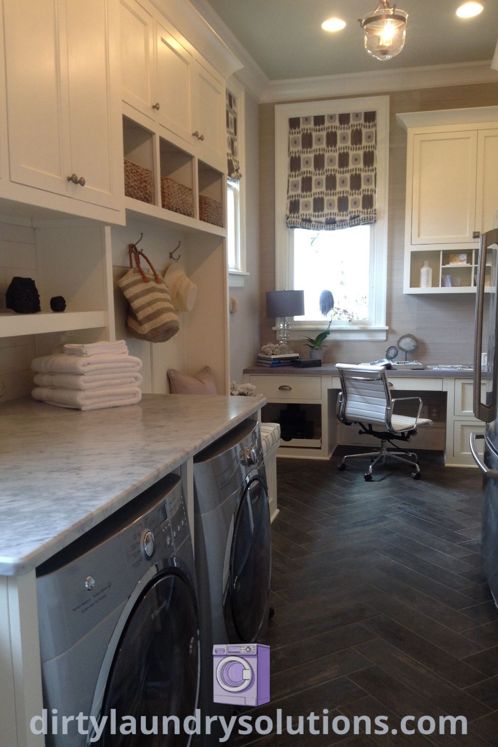 A cozy laundry room featuring a washer and dryer, white cabinetry, and a computer desk area with open shelving, combining laundry and office functions elegantly. Discover unique ideas for your home at dirtylaundrysolutions.com.