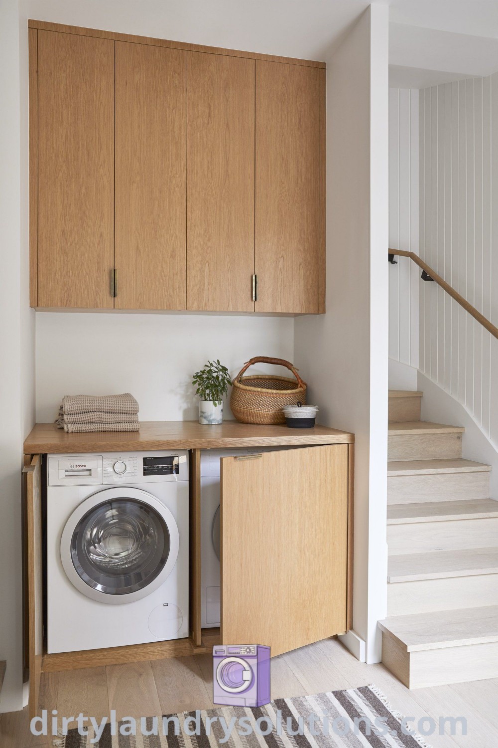 A cozy laundry area featuring a washer and dryer in a small room with stairs, beautifully designed with wood cabinets and hidden storage solutions. Discover organization ideas and inspiring laundry room decor at dirtylaundrysolutions.com.