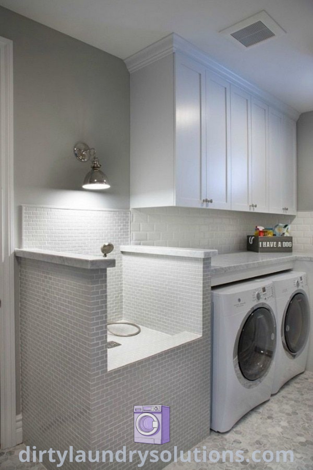 A modern laundry room featuring a washer and dryer in a white setting with gray tile flooring and functional storage shelves. The design includes a cozy wash station perfect for dogs, showcasing practical organization ideas and decor inspirations. For more unique ideas, visit dirtylaundrysolutions.com.