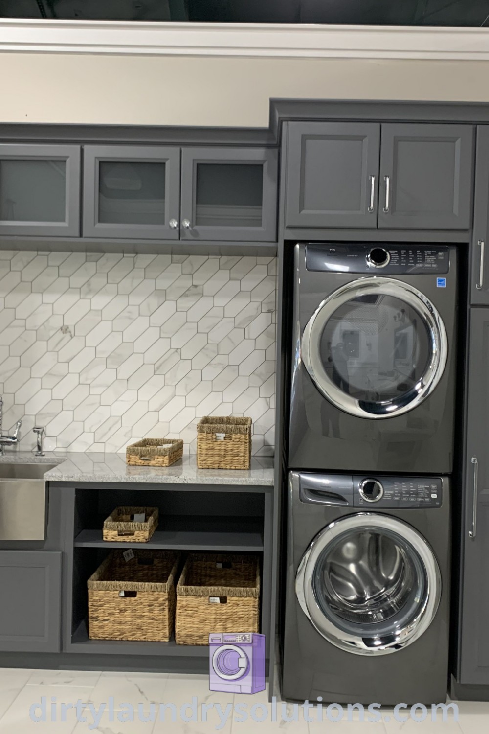 A modern laundry room featuring a gray cabinetry layout with a washer and dryer, complemented by stainless steel appliances, designed for optimal organization. For more inspiring laundry room ideas, visit dirtylaundrysolutions.com.